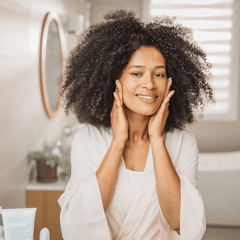 Woman applying skincare in bathroom mirror.