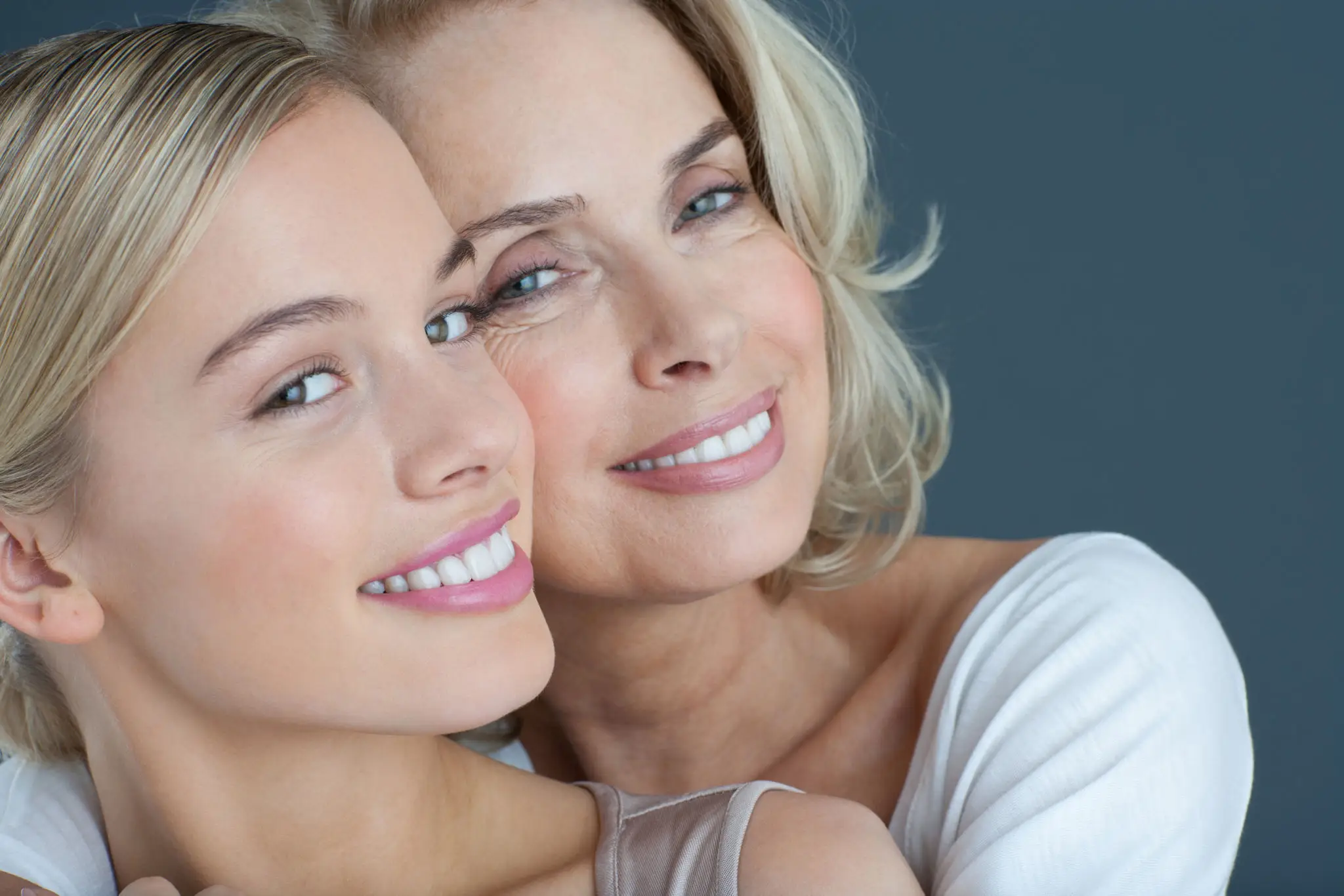 Smiling women embracing against a gray background.