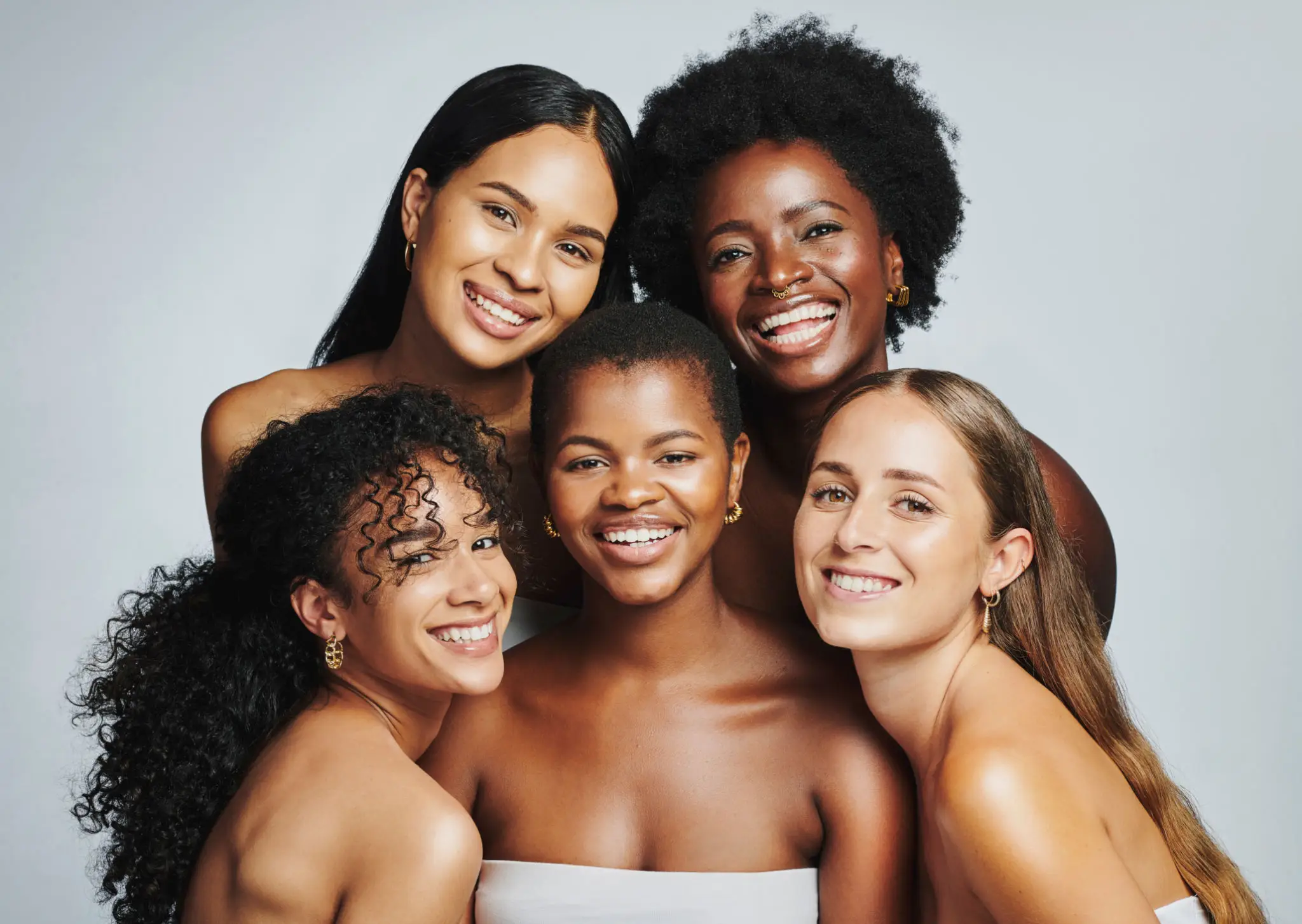 Five women smiling together, diverse backgrounds.